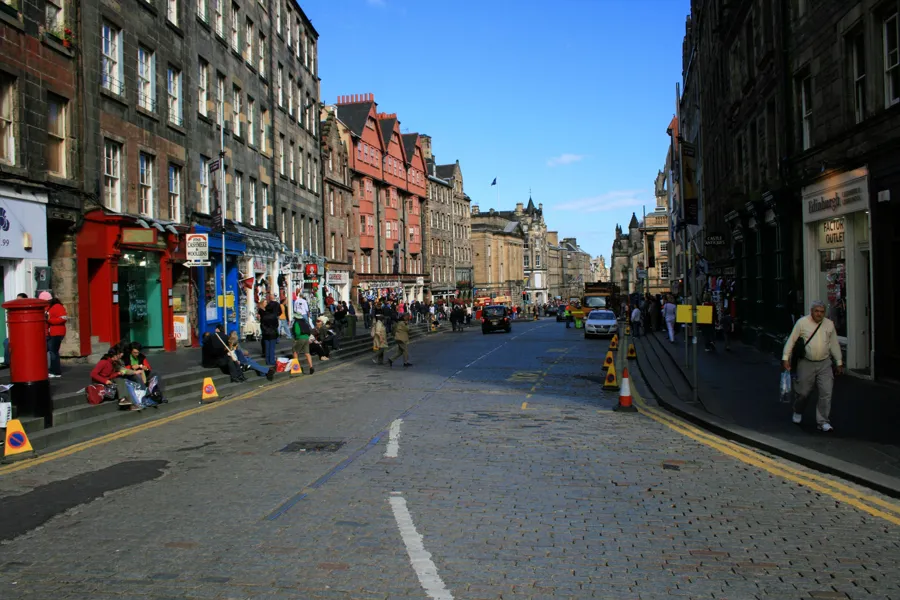 Royal Mile in Edinburgh mit hohen Steinfassaden, bunten Ladenfronten und Fußgängern an der Straße.