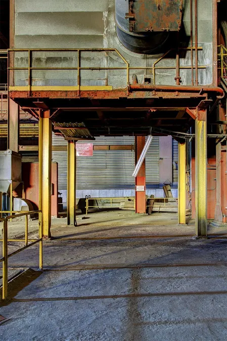 Empty passage beneath a heavy installation on yellow and red supports.