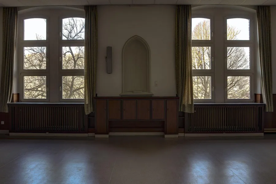 Lege kamer met twee hoge ramen en een kleine altaarnis ertussen.