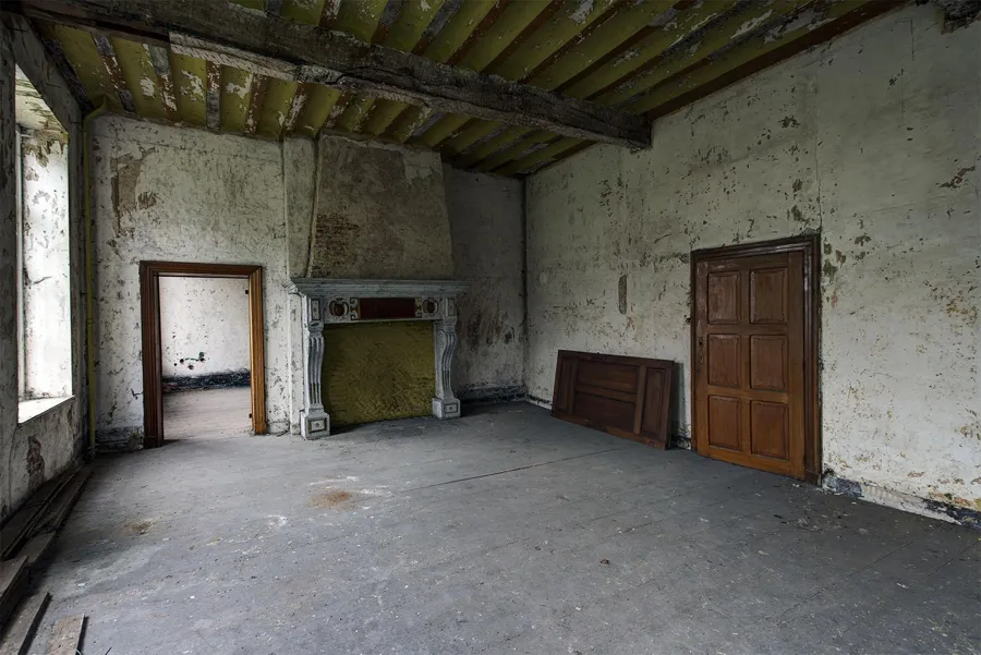 Habitación vacía con chimenea, vigas vistas y paredes deterioradas