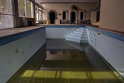 Steps into the empty indoor pool with green residual water.