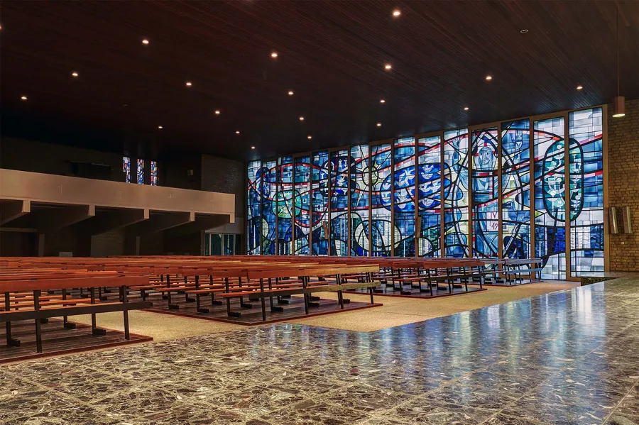 Angled view of long pews before the large glass wall beneath a dark wooden ceiling.