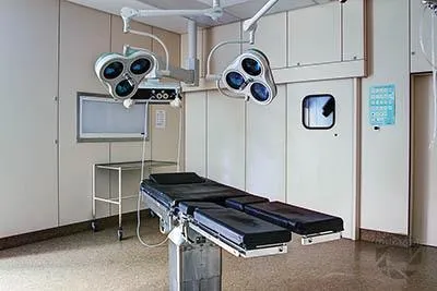Black operating table beneath two lights before double doors.