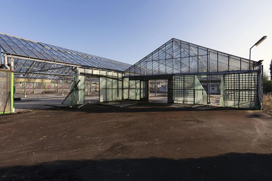 Glazen gevel van het verlaten tuincentrum met geopende groene deuren.