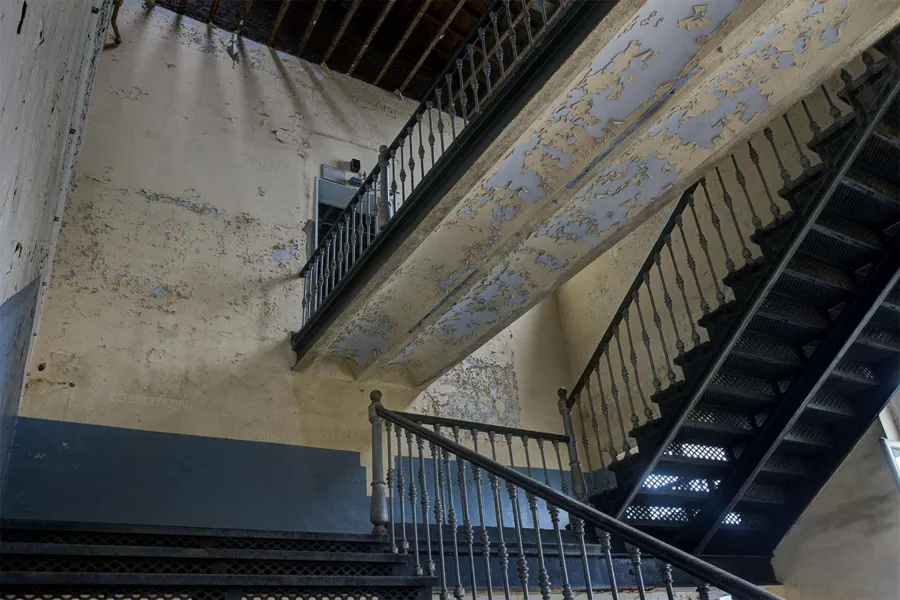 Treppenhaus mit Metallstufen und Geländern unter beschädigter Decke.