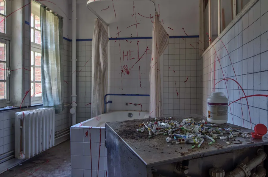 Emballages épars sur une table dans une pièce carrelée aux graffitis rouges.