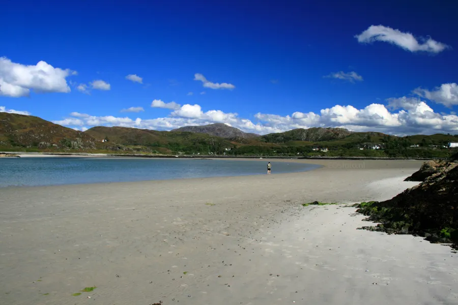 Breiter heller Sandstrand bei Morar mit flachem blauem Wasser und grünen Hügeln am anderen Ufer.