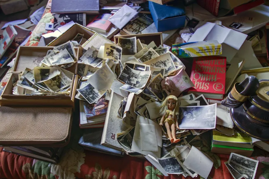 Fotografías sueltas, libros y una muñeca entre objetos abandonados