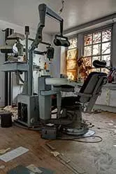 Sillón dental antiguo con equipos junto a una ventana grande.