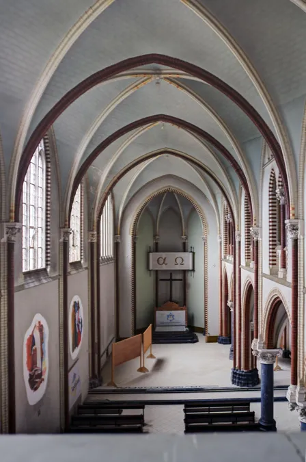 Hoge kloosterkapel met spitsgewelven, muurbeelden en een altaar achteraan.