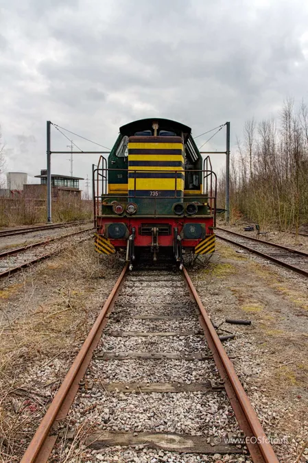 Vooraanzicht van een groen-gele locomotief op roestige rails.