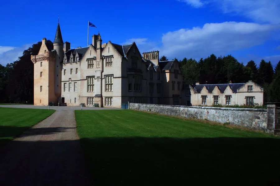 Helle Fassaden und runde Ecktürme von Brodie Castle hinter gepflegtem grünem Rasen unter blauem Himmel.