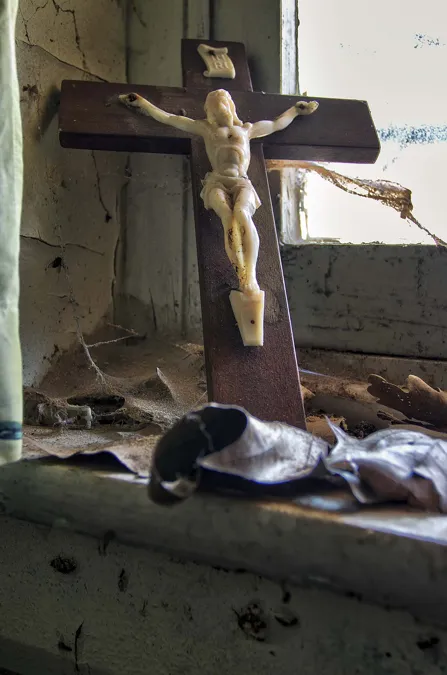 Crucifix en bois sur un rebord de fenêtre poussiéreux à la peinture écaillée.