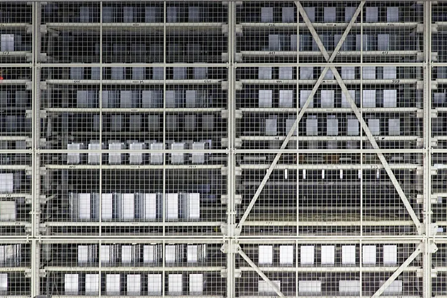 Quadrillage abstrait de grilles et passerelles métalliques traversé par un renfort diagonal.