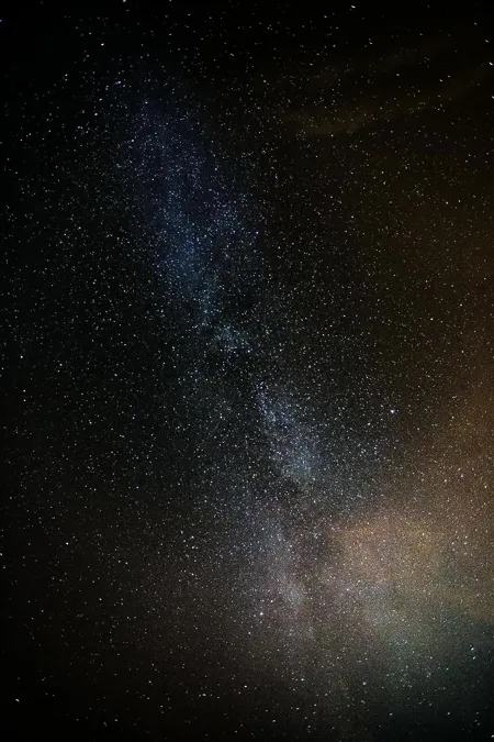 Vertical view of the Milky Way as a pale, cloudlike band among countless stars in a dark night sky.