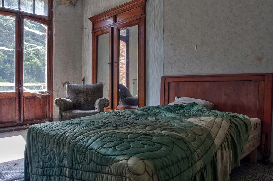 Bed with a green bedspread and armchair beside wooden doors.