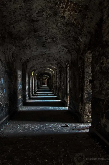 Long dark corridor with repeated arches and side openings.