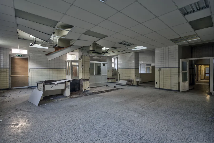 Cocina industrial deteriorada con campanas extractoras y paneles de techo ausentes.