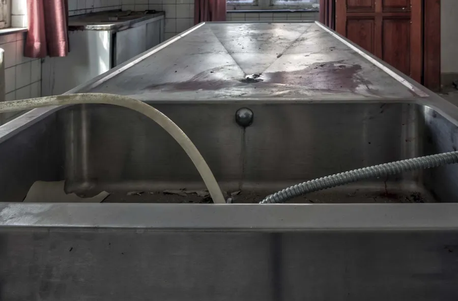 Table métallique avec bac profond et tuyaux souples dans une pièce carrelée.