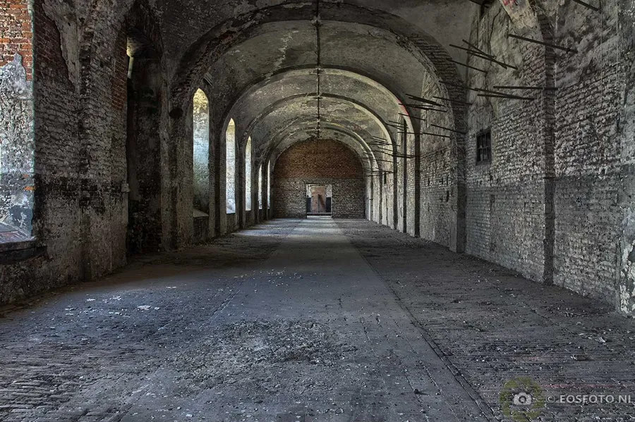 Wide empty brick corridor with vaults and tall windows.