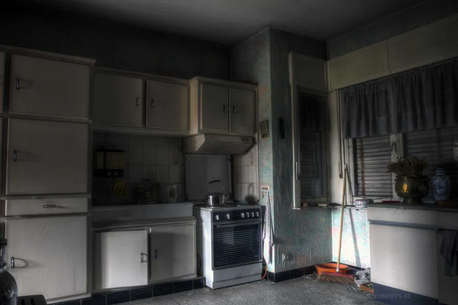 Alte Küche mit weißen Schränken, Herd und Kühlschrank.