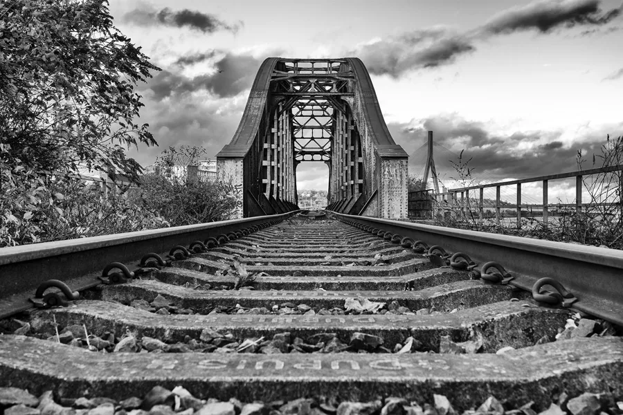 Laag breed zicht langs spoorrails naar een hoge stalen spoorbrug.