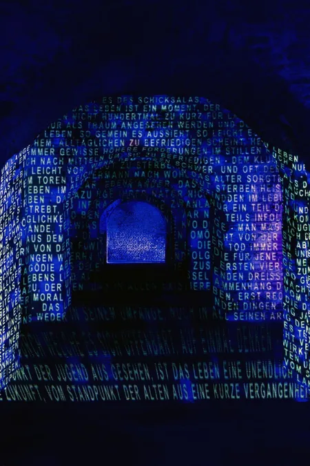 Woorden geprojecteerd op een donkere bakstenen booggang in blauw licht.