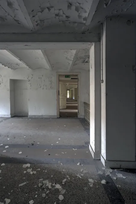 Sala vacía con puertas abiertas y escombros en el suelo.