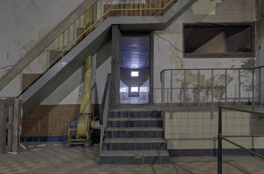 Kurze Treppe mit Metallgeländern zu schmaler Tür unter einer schrägen Treppenkonstruktion.