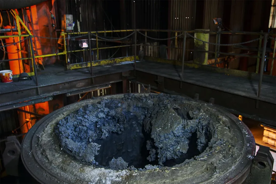 Thick encrusted rim of an open circular furnace vessel.