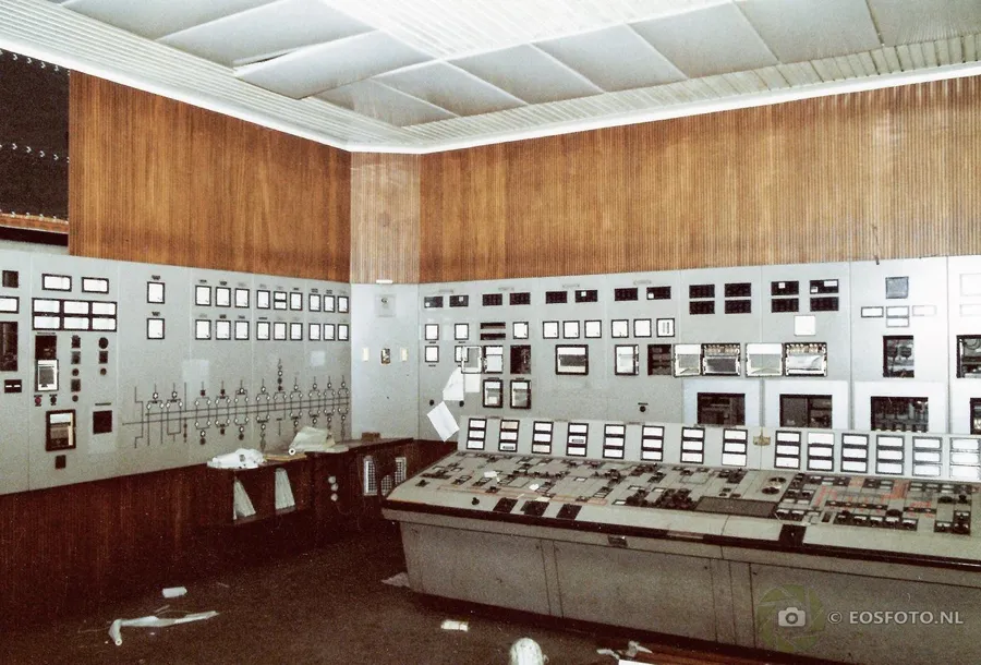 Sala de control con paredes de madera y paneles largos de medidores e interruptores.