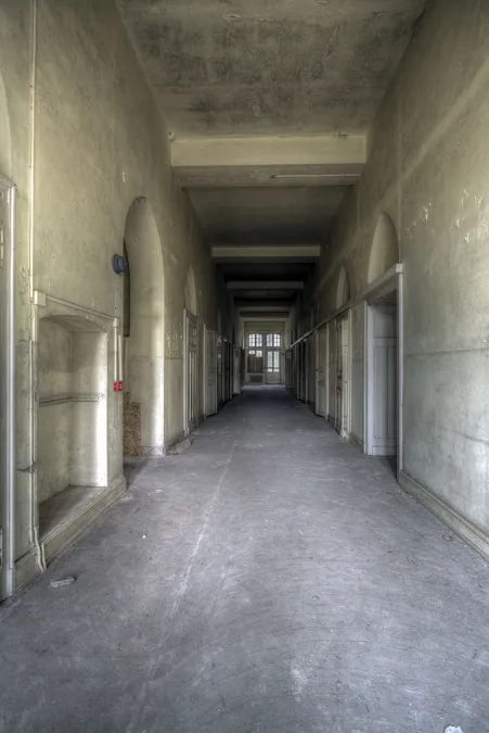 Pasillo largo vacío con techo plano y ventanas luminosas a la izquierda.