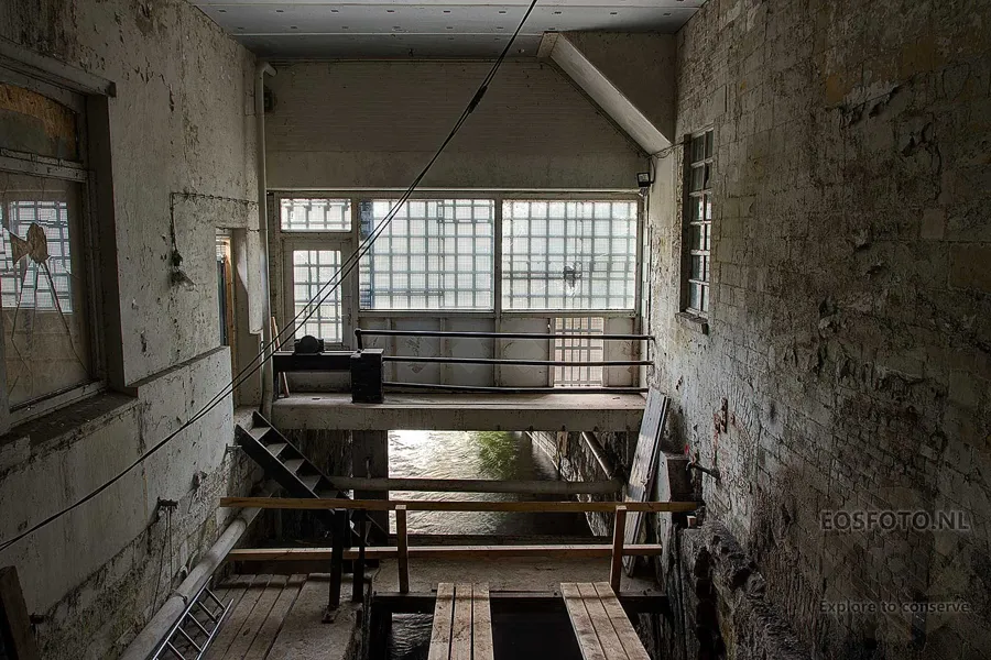 Empty industrial space with an open floor and narrow walkway before a large window.