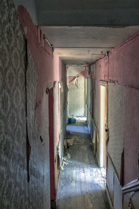 Narrow pink corridor with a damaged timber floor.