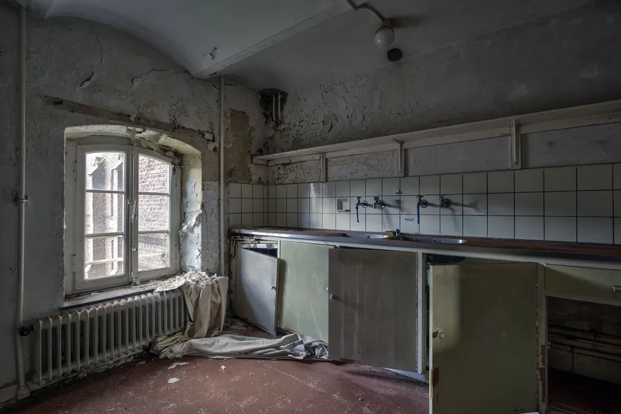 Cocina antigua con armarios bajos verdes, azulejos blancos y ventana izquierda.
