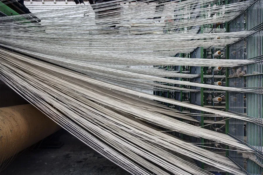 Haces de hilos blancos se abren desde un rodillo textil ancho.