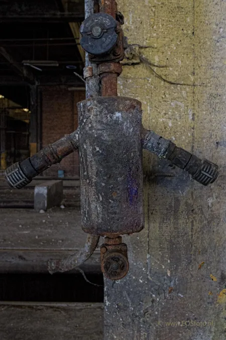 Roestige metalen aansluitkast met twee zijuitgangen op een betonnen kolom.