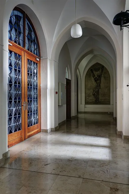 Gewelfde gang met brede glasdeur links en religieuze schildering achterin.