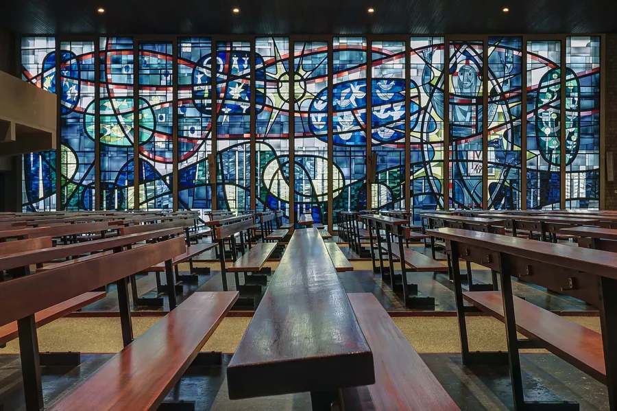 Large blue, red and green stained-glass wall behind long wooden pews.