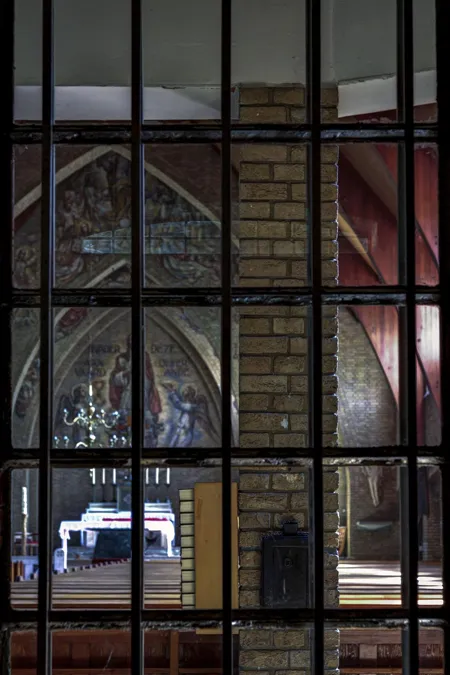 View through black metal bars towards pews and painted walls inside the church.