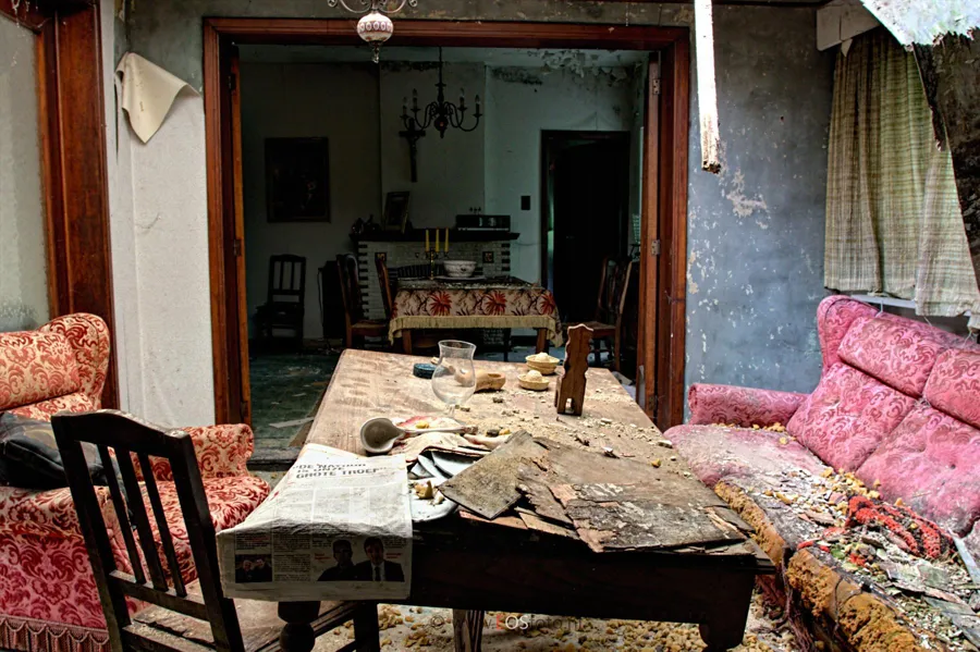 Damaged table with crockery between a worn sofa and chairs