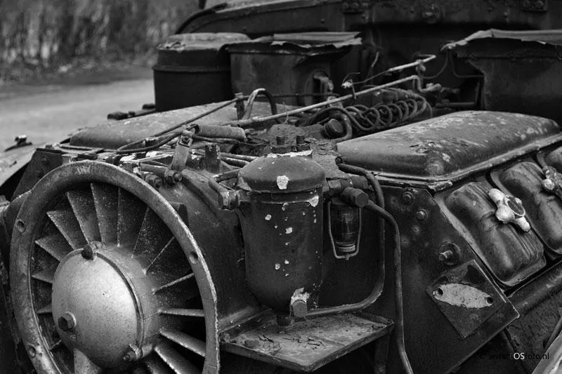 Alter Motor mit großem Lüfterrad und Leitungen, in Schwarzweiß fotografiert.
