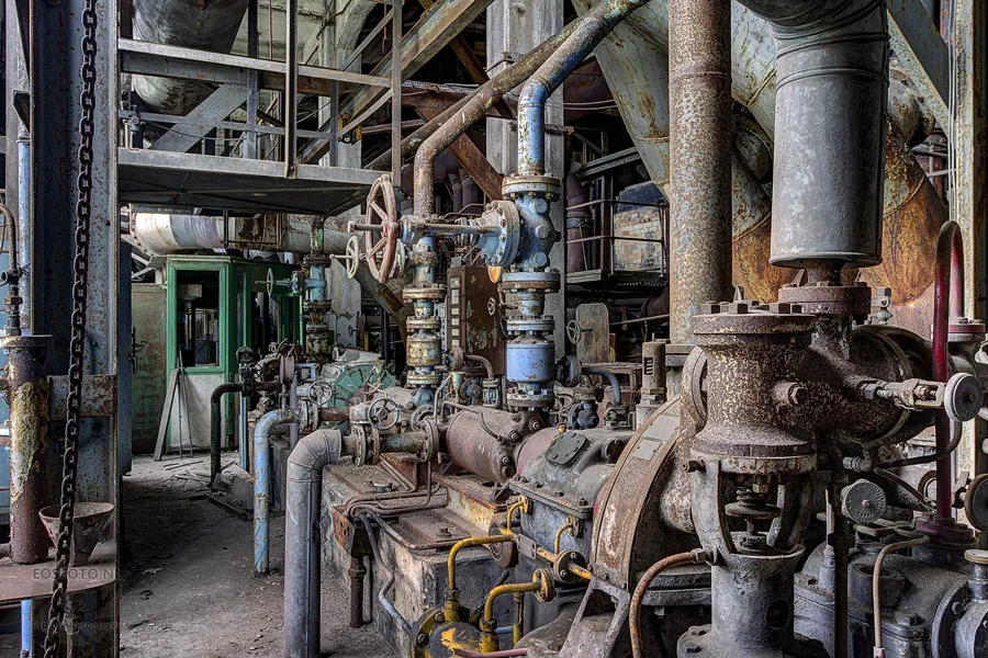 Numerous rusty pipes and valves between heavy machine parts.