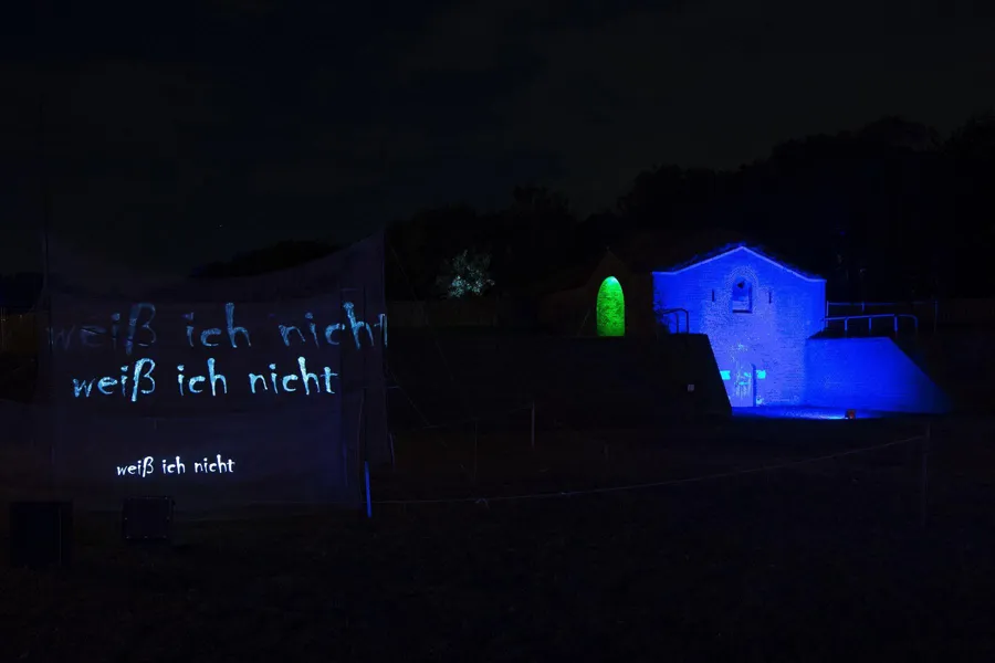 Witte tekstprojectie vooraan met een blauw verlicht gebouw op de achtergrond.
