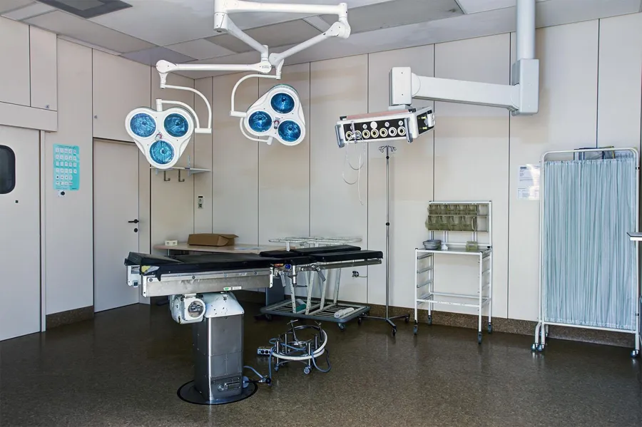 Mesa de operaciones con dos lámparas azules y biombo.