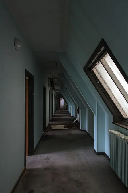 Pasillo azul estrecho de ático con ventanas inclinadas y puertas izquierdas.