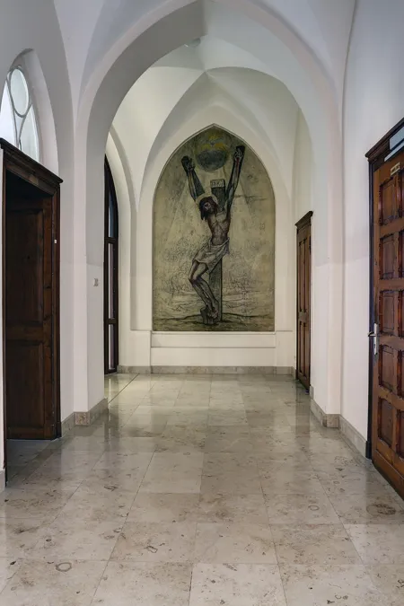 Einde van een gewelfde gang met grote schildering van de gekruisigde Christus.