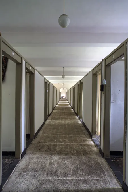 Pasillo recto con larga fila de espacios para dormir separados y lámparas colgantes.
