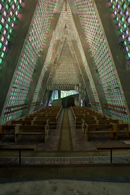 Interior triangular alto de iglesia con bancos de madera y paneles verdes y rosas.