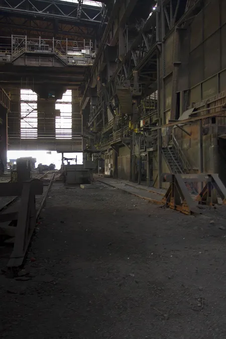 Dark tall factory hall with pipes and daylight at the far end.